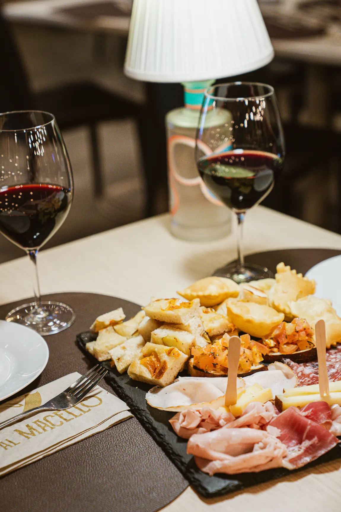 Tagliere di aperitivo su ardesia con salumi, focaccia, bruschette e due calici di rosso